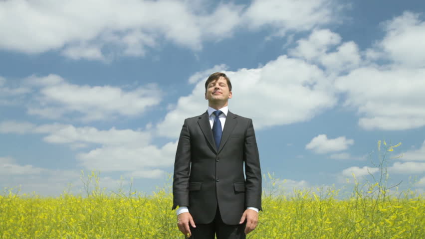 Young businessman standing in the field with his eyes shut enjoying trouble-free life