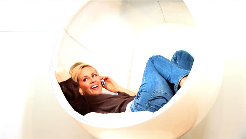 Beautiful blonde girl using her mobile phone sitting in retro circular chair