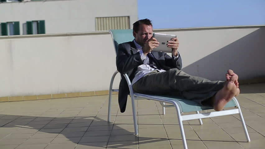 Angry businessman with tablet computer on sunbed, slow motion
