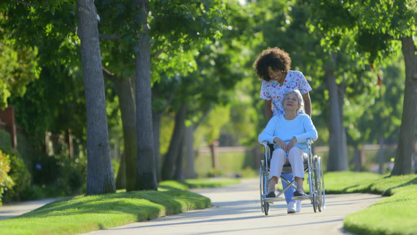 Nurse walking with elderly woman in wheelchair