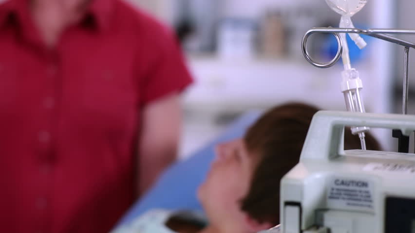 Camera tracks around to reveal boy lying in hospital bed listening to comforting words from his doctor.