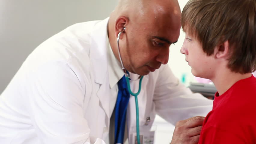 Camera tracks around then tilts down as a doctor of Indian heritage checks the lungs and breathing of young boy.