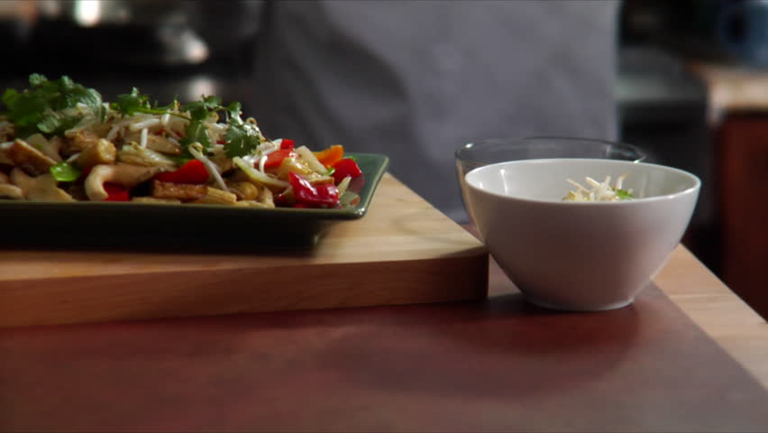 Slow pan over a plate of Asian stir fried vegetables with chef flaming wok in background and pan landing on statue of Buddha.