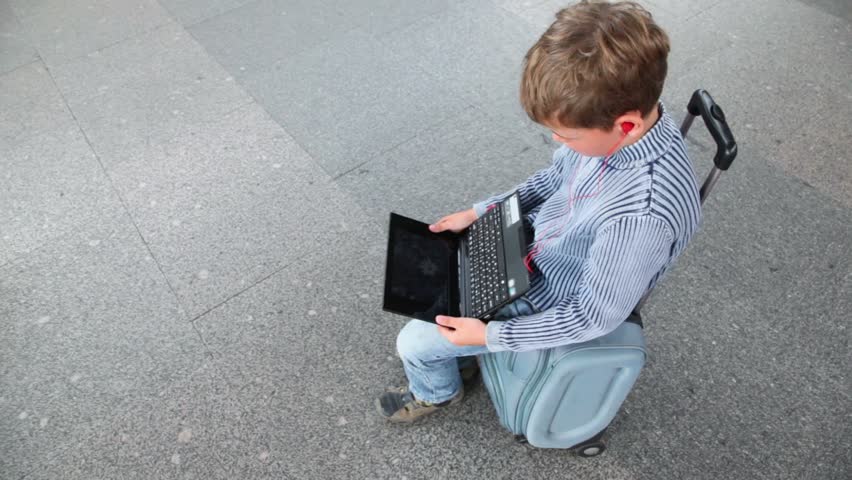 Little boy hold netbook when sits on travelling bag