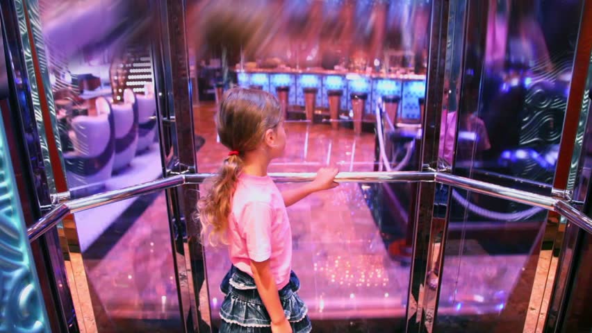 Little girl stands in elevator with transparent glass walls which lifts from restaurant