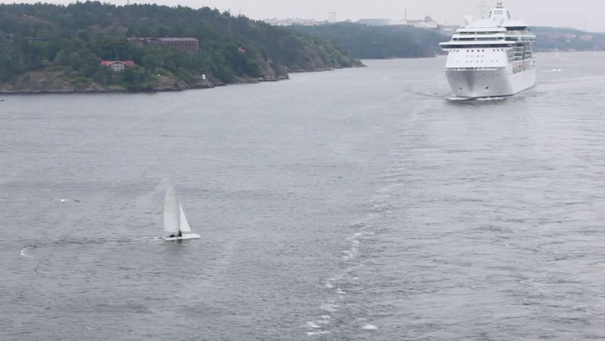 Yacht and cruiser float in sea near coast with houses among forest