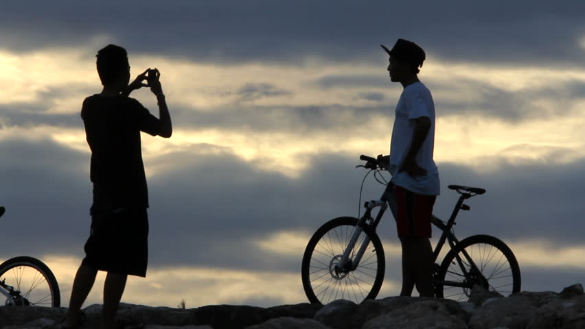 boys take pictures with cellphone on mountain after long bike ride 