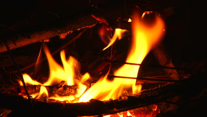Unrecognizable woman sitting at campfire at night zoom out.