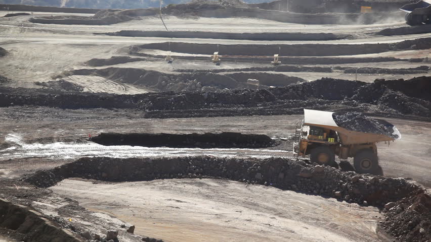 Heavy equipment digs and hauls ore inside an enormus open pit mine.
