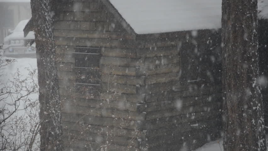 slow pan across the front of a  mountain cabin in a severe winter snowstorm