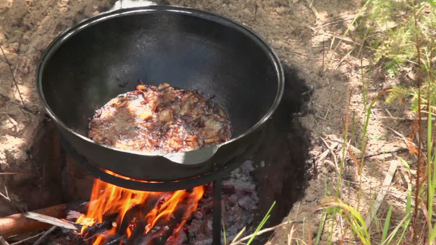 Broiled onion with meat boils in hot oil at pot on campfire