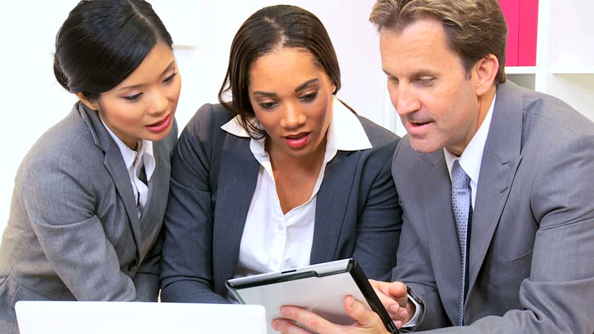 Three young multi ethnic business colleagues in close up using wireless technology informal meeting