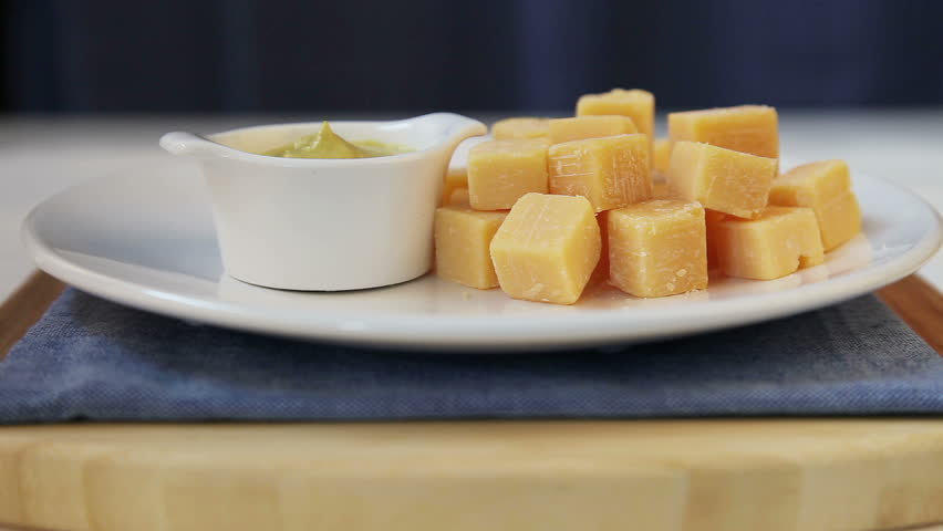 Appetizer of cheese cube being dipped in spicy mustard