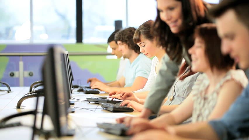 Class of male and female young students working on computer with Caucasian lecturer in college information hub