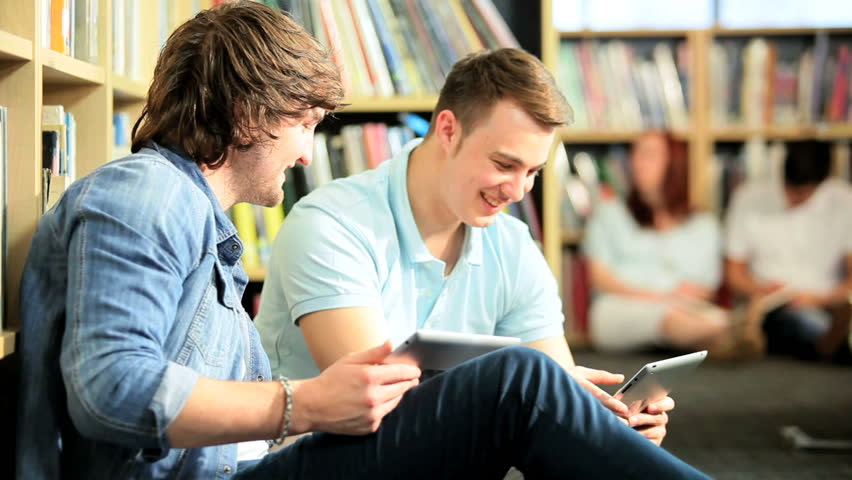 Caucasian young male students networking on tablets in university library