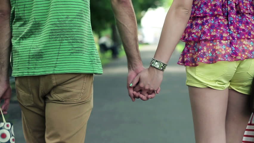 Couple holding hands and walking in the park, steadicam shot
