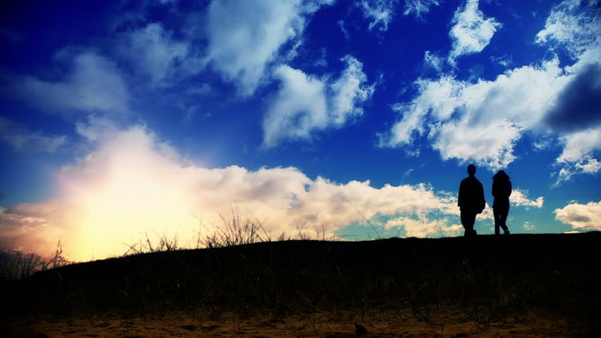 Couple walking on green meadow at sunset, time lapse clouds