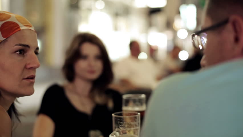 Three friends in restaurant drinking beer in the evening, steadycam shot
