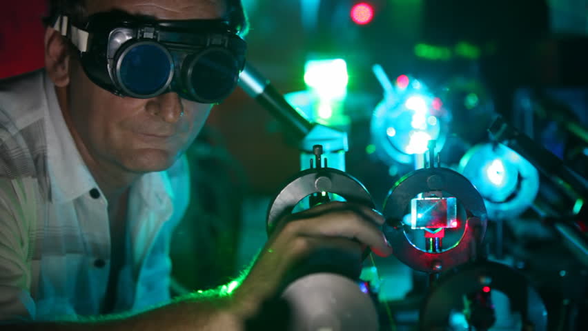 scientist in goggles twists handles of devices of laser and magnifying glasses close up