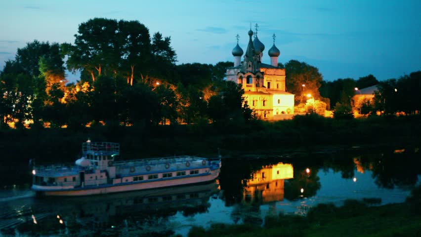 Ship sails down river near coastal church with illumination at night