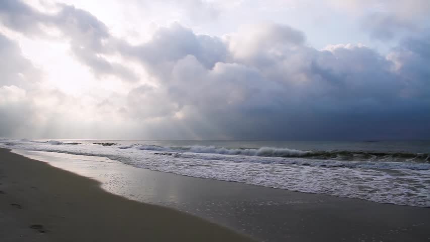 HD loop features a sandy beach with breaking waves and sunbeams penetrating clouds above.
