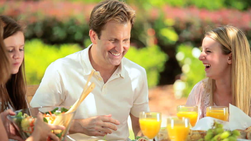 Parents providing young daughters with sensible healthy low fat lunch food in home garden