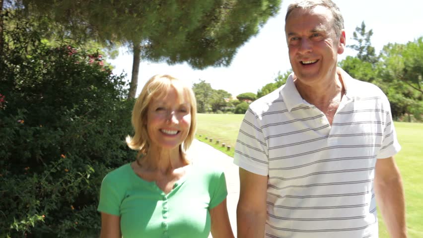 Romantic senior couple holding hands as they walk along country path.