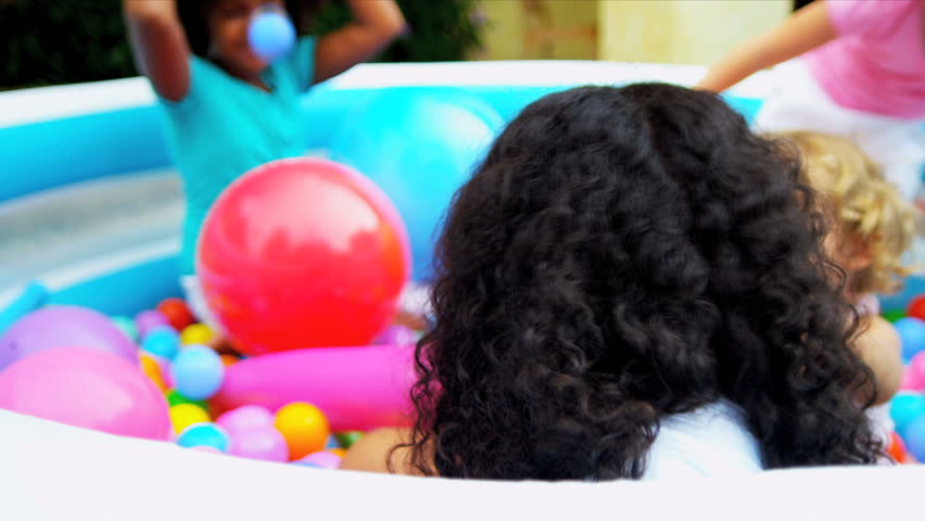 Pretty young ethnic girl in forefront having fun playing with friends in multi coloured ball pool shot on RED EPIC