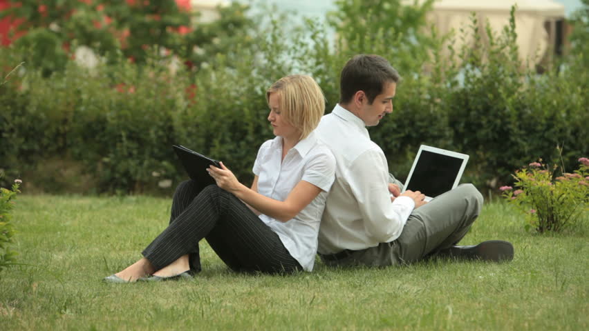 Young business people sitting back to back on the grass, working and talking