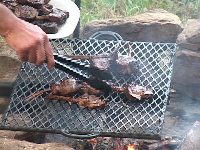Grilled lamb chops being turned and removed from the fire