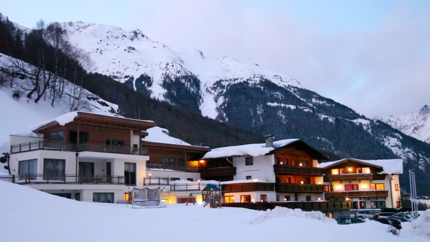 Chalets stand against mountain landscape in evening light of lamps