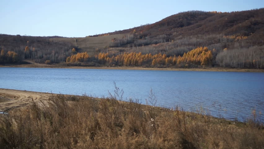 Panoramic view of the Wo Niu Hu lake in northern China. Hilly coastline, covered with colorful autumn forest, water surface, reflecting the blue sky. Panning right. October 2012. 