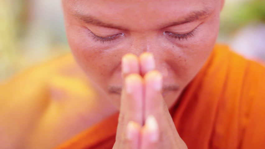 Buddhist monk with orange robe pray in temple with hands clasped 
