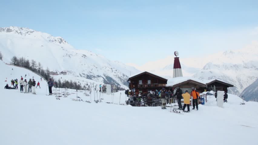 People ride ski and snowboards near rest house with rows of benches