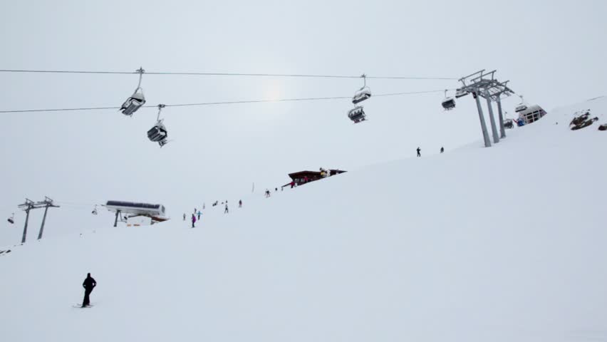 People ride ski and snowboards near cableway on Austrian Alps at winter day