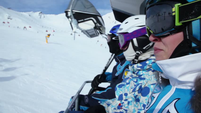 One of three skiers shows something by finger during ropeway ride at mountains