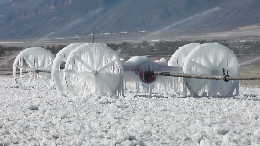 Frozen ice on farm field irrigation sprinkler system. Farm irrigation sprinkler in farmer field after first freeze snow and ice. Aluminum wheel frozen early winter storm cold weather.  Agricultural.