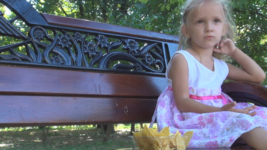 Little Girl Eating Cornflakes on a Bench in Park