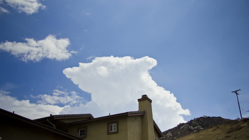 A storm cloud builds in time lapse over a house in the hills. Illustration of a storm moving in, the weather transitions from sunny to very dark