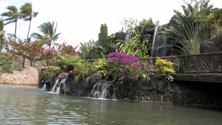 Polynesian canoes moving across a tropical pond in Oahu, Hawaii. Palm trees and waterfalls. 