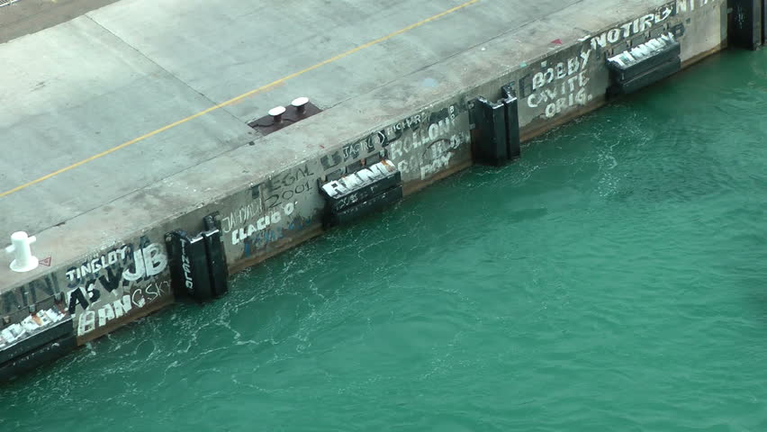 A ship is leaving the harbor moving away from the jetty, on which we can see the "signatures" of the painters assigned to the cleaning of the ship walls