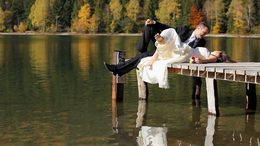 Bride and groom having a romantic time together on a pontoon over a mountain lake with an amazing autumn scenery in the background