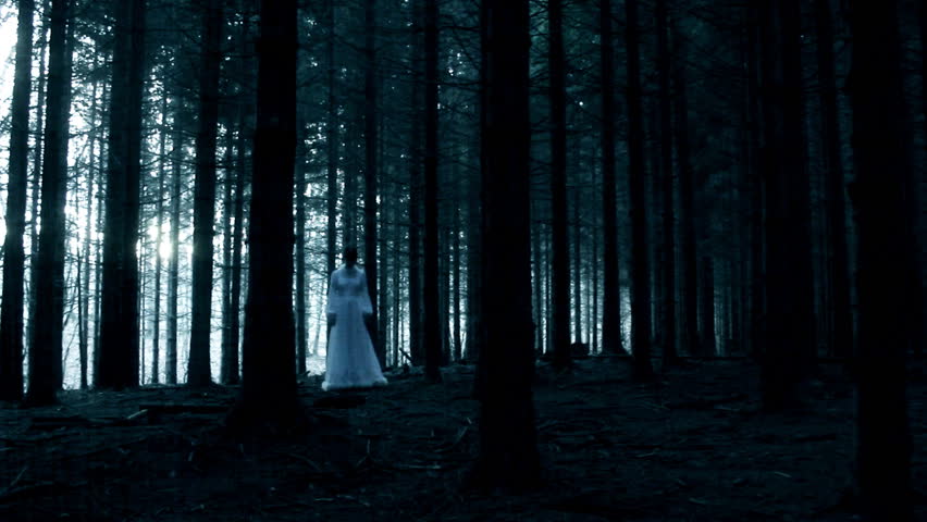 Mysterious woman in the white dress in walking in the dark spooky forest