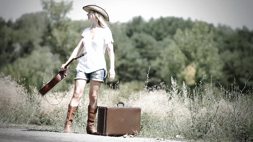 Young woman with guitar on the road and her vintage baggage