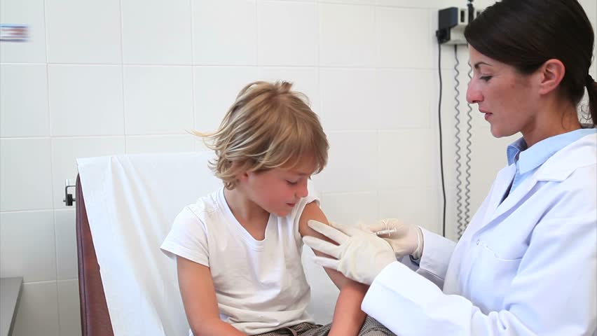 Doctor injecting liquid in a child arm in examination room
