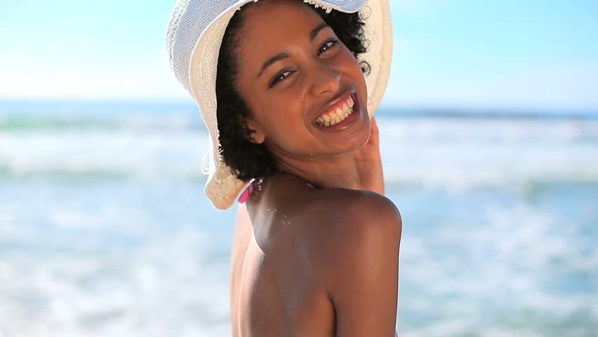 Happy brunette woman wearing a straw hat on the beach