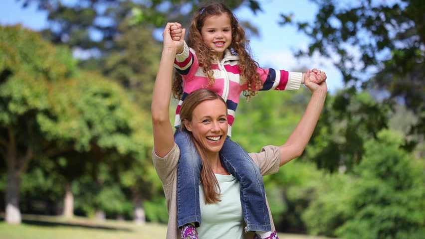 Woman turning with her daughter on her shoulders in a park