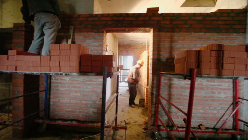 Two workers build partition between rooms at construction site, panoramic motion