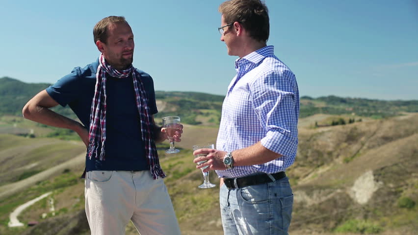 Two male friends celebrating and drinking outdoors, crane shot

