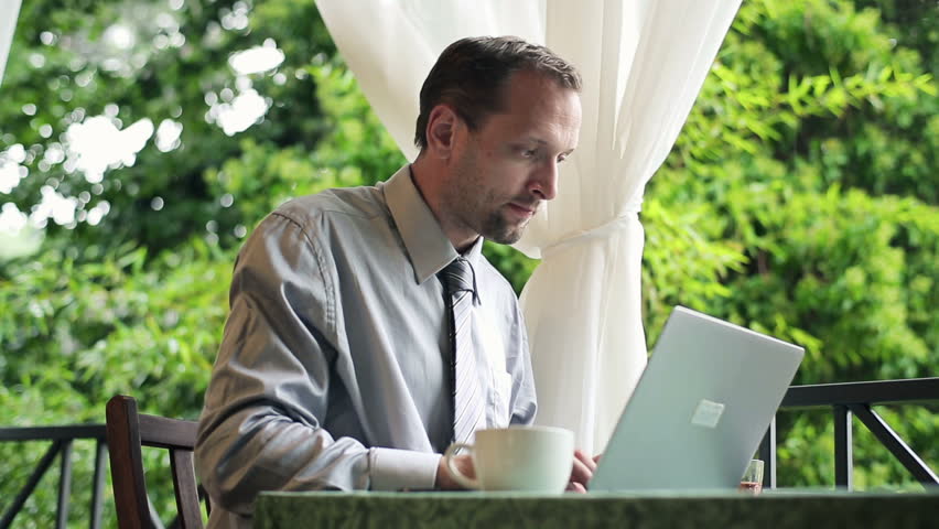 Businessman working on laptop and drinking coffee on balcony
